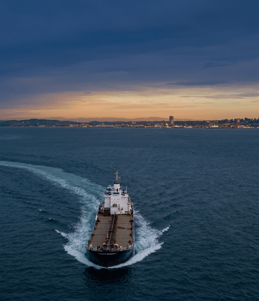 Cargo vessel underway with a trailing wake and a distant coastal skyline